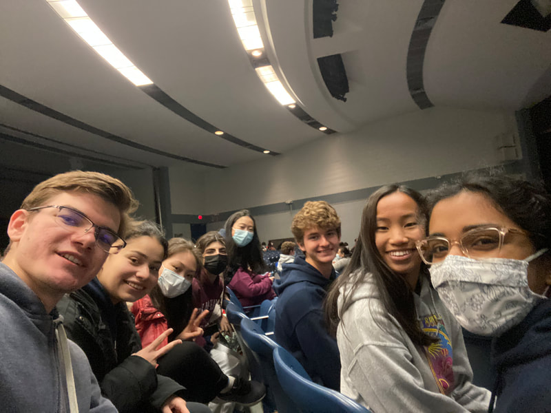 A group of students sit in an auditorium, smiling at the camera. 
