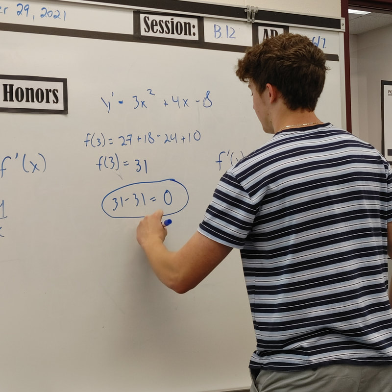 A student with their back turned to the camera solves a math problem on the whiteboard. 