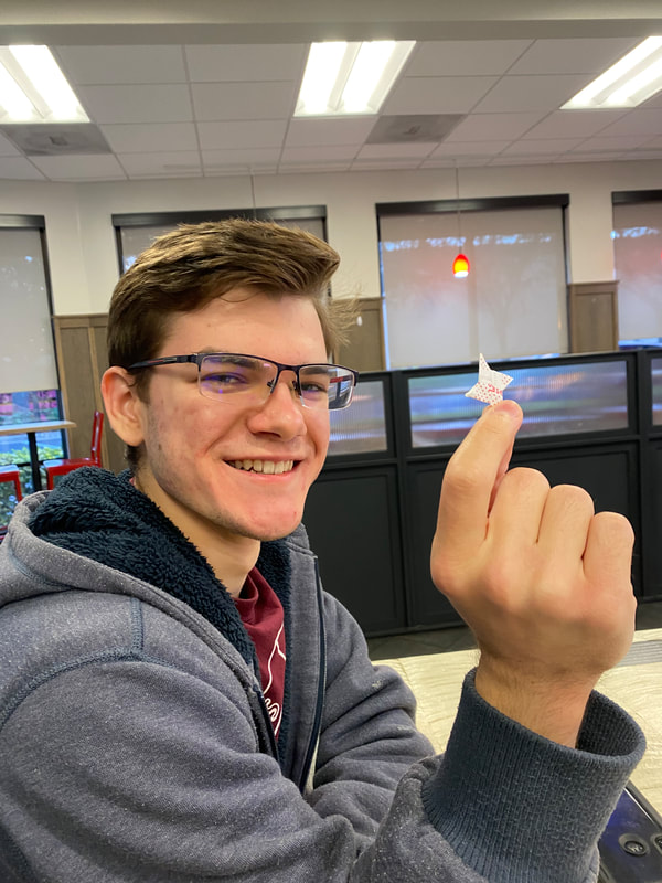 A student holds up a origami ninja star in his right hand. 