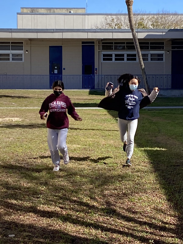 Two students run happily on a grass field. 