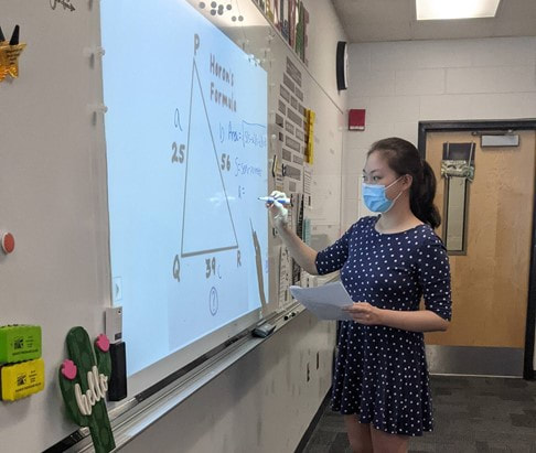 A student writes on a whiteboard displaying a triangle with labeled parts. 